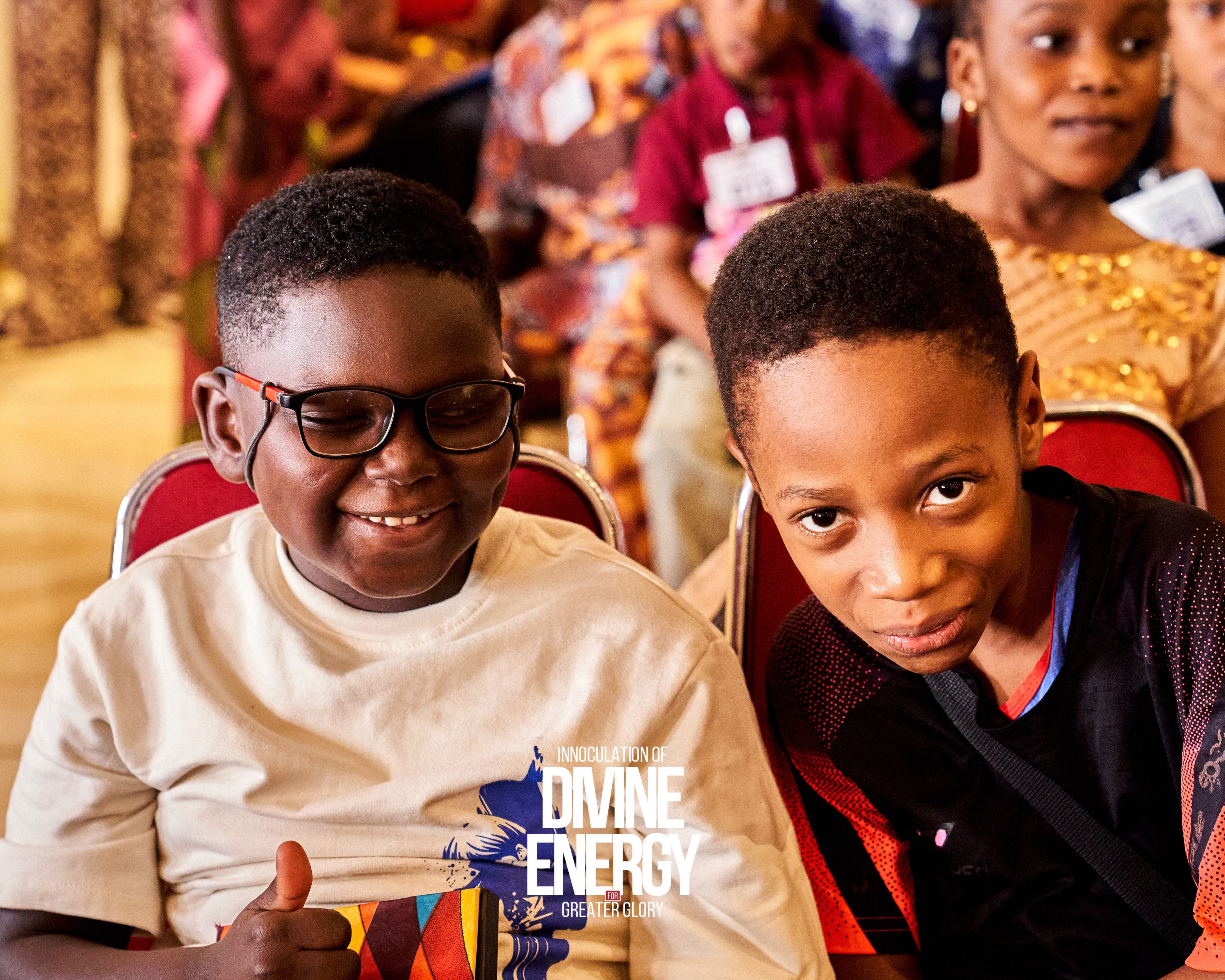 Two boys smiling during children's service, one giving a thumbs up